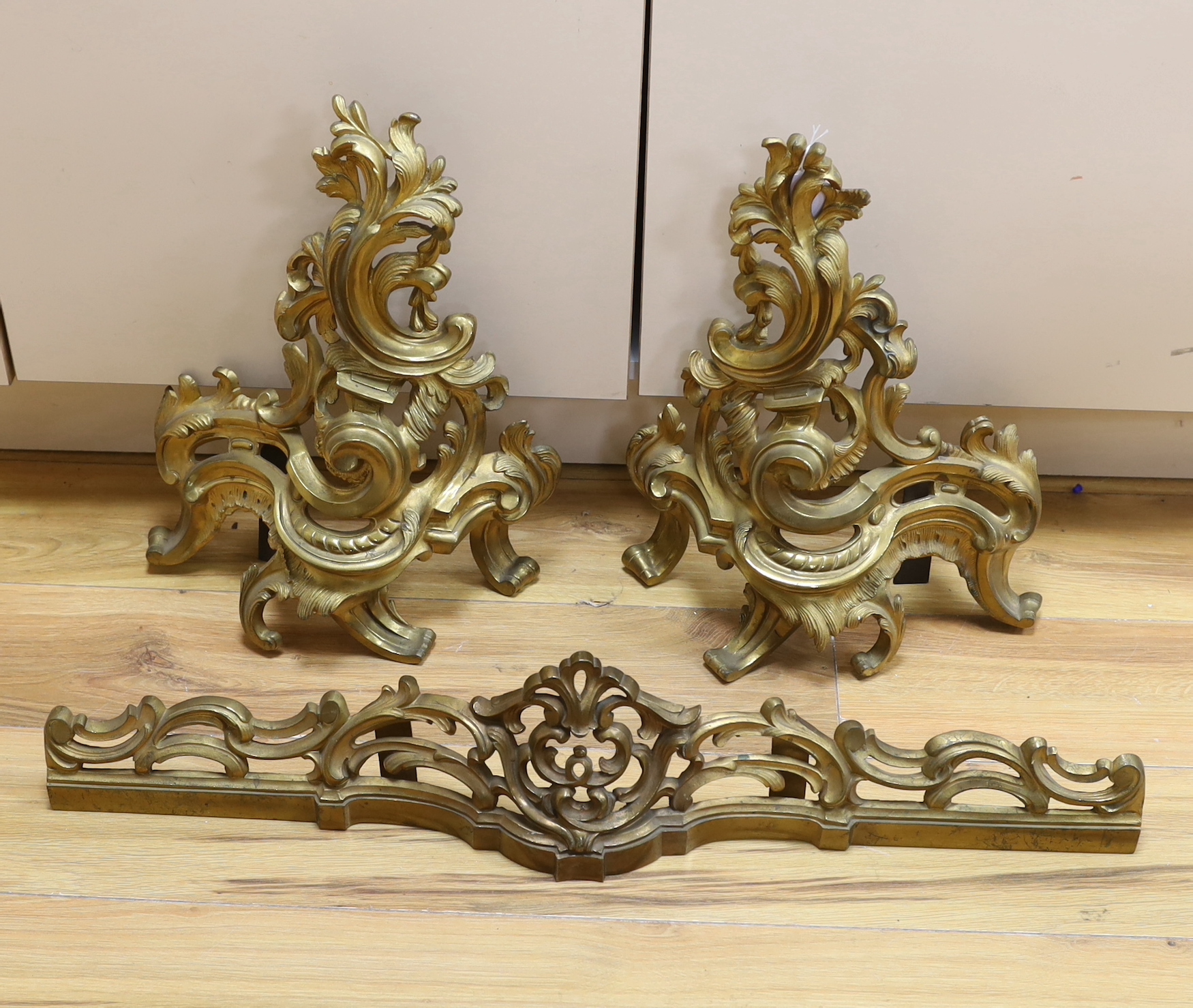 A French rococo revival gilt bronze fender with scroll work and bar, largest 44cm high